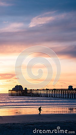 Vertical shot of a silhouette of a pier and a person walking at the beach during sunset Stock Photo