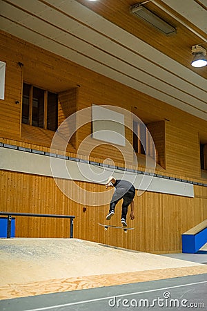 Vertical shot of a skateboarder jumping over the skating ramp inside a building. Stock Photo