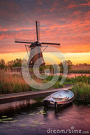 Vertical shot of a small boat in a lake and a mill in the background under the cloudy sunset sky Stock Photo