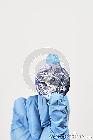 Vertical shot of a small globe in the hand of a person in a blue plastic glove Stock Photo