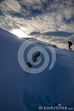 Vertical shot of a snowy hillside with a person trekking and bright sun shining over Stock Photo