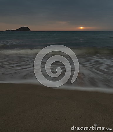 Vertical shot of waves on the coastline with the sun setting in the background Stock Photo