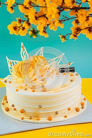 Vertical shot of a white birthday cake with a yellow rose on it and orange flowers background Editorial Stock Photo