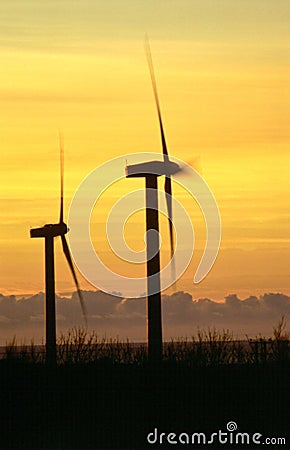 Vertical shot wind turbines silhouetted against the orange sky at sunset Stock Photo