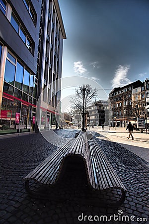 Vertical shot of a wooden bench next to a building under a cloudy sky Editorial Stock Photo