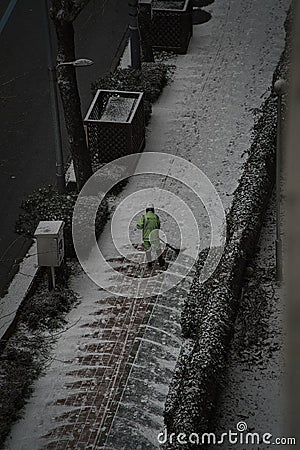 Vertical shot of a worker cleaning the snow off the paved sidewalk with a shovel Editorial Stock Photo