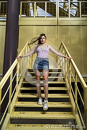 Vertical shot of a young caucasian female posing while standing on the yellow stairs of a building Stock Photo
