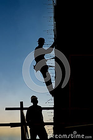 Vertical silhouette of a construction worker in harness on the side of a buiilding under construction Stock Photo