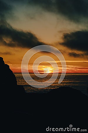 Vertical of the silhouettes of beach rocks and a dark seascape captured at sunset Stock Photo