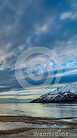 Vertical Striking cloudy sky over a calm lake that reflects the golden sun at sunset Stock Photo