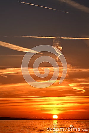 Vertical sunset over the sea with plane trails and clouds Stock Photo