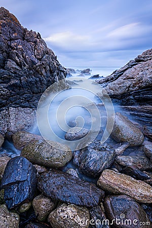 A vertical sunset seascape photograph of misty waves crashing on the rocks Stock Photo