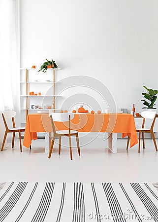 Modern interior. Long dining room table with chairs. White walls and floor, orange details. Real photo concept Stock Photo