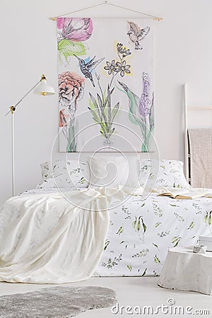 Vertical view of a scandinavian style bedroom interior with a bed dressed in white linen with painted green plants. Fabric wall ar Stock Photo