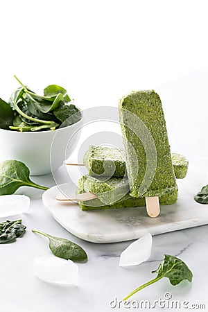 Vertical view of a stack of green smoothie popsicles with one standing in front and a bowl of spinach in behind. Stock Photo