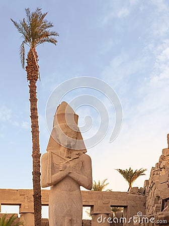 Vertical view of the statue of Ramses II in the temple of Amun-RA in Karnak, Egypt with a palm tree behind Stock Photo
