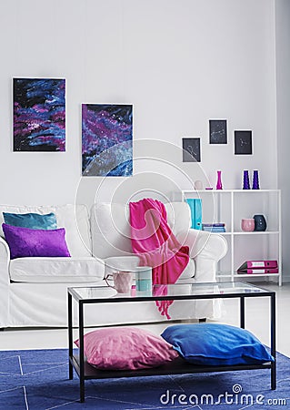 Vertical view of stylish living room with comfortable white couch with pink blanket and blue and purple pillows, cosmos graphics o Stock Photo