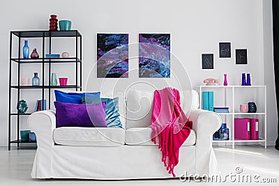 Vertical view of stylish living room with comfortable white couch with pink blanket and blue and purple pillows, cosmos graphics o Stock Photo