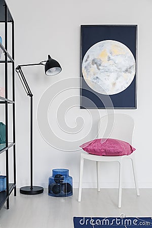 Vertical view of white chair with pink pillow in white interior with moon graphic on the wall and metal lamp, real photo Stock Photo