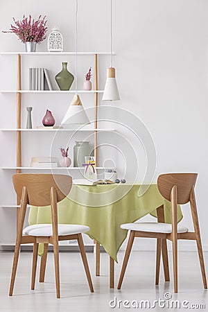 Wooden chairs at round table with olive green tablecloth in bright elegant living room, real photo Stock Photo