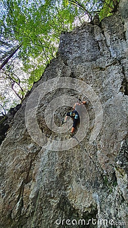 VERTICAL: Young athletic woman top rope climbs up challenging cliff in Slovenia. Stock Photo