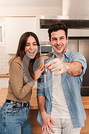 Vertical Young caucasian couple happy to show the keys of their new home looking at camera together, Smiling husband and Stock Photo