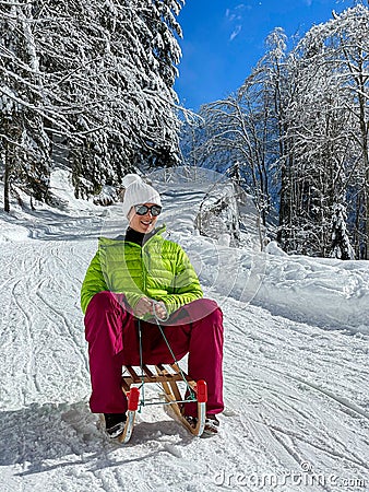 VERTICAL: Young Caucasian woman sleds down a groomed slope in the sunny Alps. Stock Photo