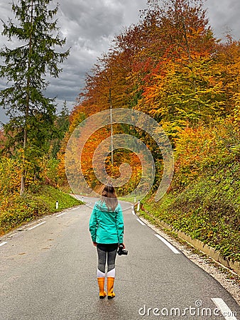 VERTICAL: Young female photographer stands in the middle of a forest road. Stock Photo