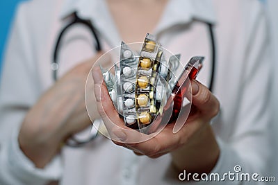 Vertically folded packs with different pills in a woman`s hand and a stethoscope around her neck Stock Photo