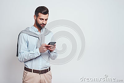 Very busy. Handsome young man in casual wear using his smart phone while standing on a grey background. Digital concept Stock Photo