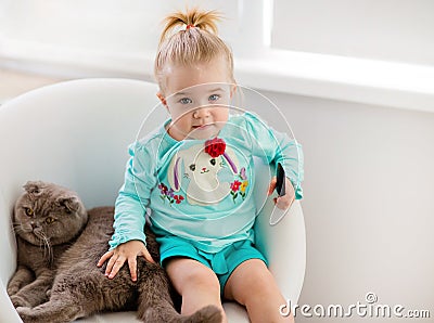 Very cute little girl in the blue jacket sits on the chair with Stock Photo