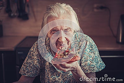 Very elderly woman eating a piece of pizza at home. Stock Photo