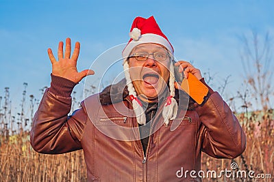 Very emotional man in funny santa hat talking on the phone Stock Photo