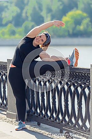 very flexible stout woman performs exercises on the embankment in the city park Stock Photo