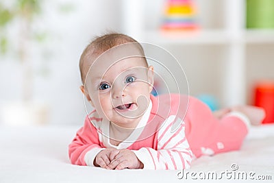 Very happy laughing baby in pink clothes lying on his belly. Infant looking straight at the camera Stock Photo