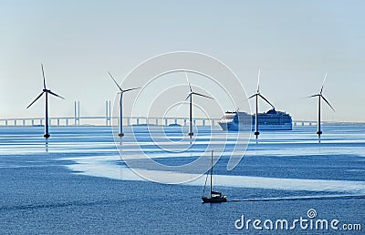 A very large passenger ship and a small sailboat pass offshore wind turbines near the Oresund Bridge between Denmark and Sweden Stock Photo