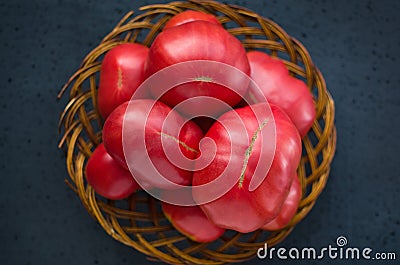 Very large ripe tomatoes in a large wicker wooden plate on a black background Stock Photo