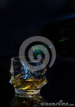 Very nice tumbler for whiskey with ice in which the golden liquid is poured from the bottle. on a black background space for text. Stock Photo