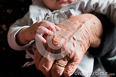 Small baby hand touching and caressing old grandmother hand with wrinkles, symbol of passing generations Stock Photo