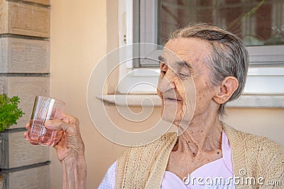 Very old senior woman in the balcony holding a glass of water in her hand Stock Photo