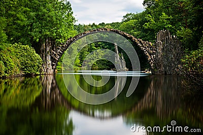 Very old stone bridge over the quiet lake with its reflection in the water Stock Photo