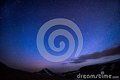 Very starry night sky, falling star, and against the background of the mountains are not yet completely freed from snow Stock Photo