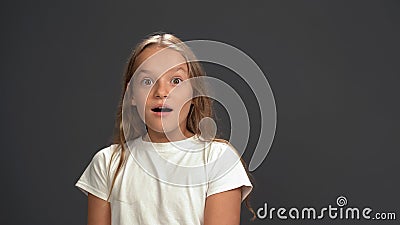 Very surprised, dumbfounded little girl looking at the camera wearing white t-shirt and black pants isolated on black Stock Photo