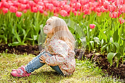 Very sweet beautiful blonde girl in a pink coat sitting near the Stock Photo