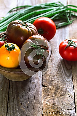 Vertical various tomatoes in clay bowl in contr light decorated with green fresh onion. Stock Photo