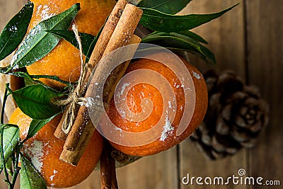 Vibrant Orange Tangerines on Branches Green Leaves Cinnamon Sticks tied with Twine Pine Cone Wood Background. Christmas Stock Photo