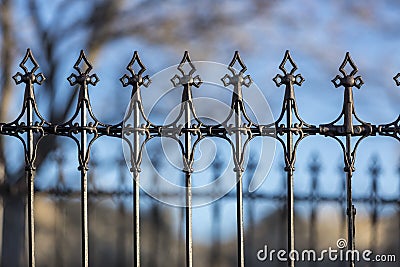 Victorian fleur de lis fence made of wrought iron with an out of focus tree branch background Stock Photo