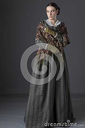 A working class Victorian woman wearing a dark green check bodice and skirt with an apron and holding a candle. Stock Photo