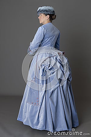 A Victorian woman wearing a pale blue velvet bustle ensemble with a fur muff and hat Stock Photo