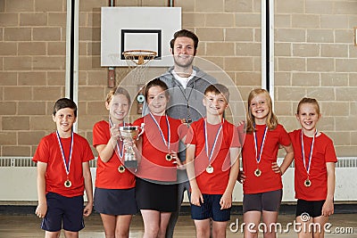 Victorious School Sports Team With Medals And Trophy In Gym Stock Photo